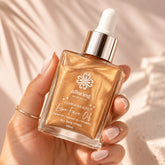 A hand holding a square glass bottle of Alluring Minerals Luminous Kiss Live Face Oil. The oil inside is a shimmering metallic gold, with a shiny silver dropper cap and white dropper bulb.