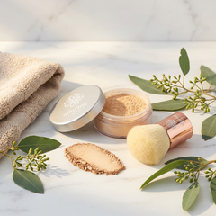 Cosmetic products including a compact, jar, and brush with green leaves on a light background