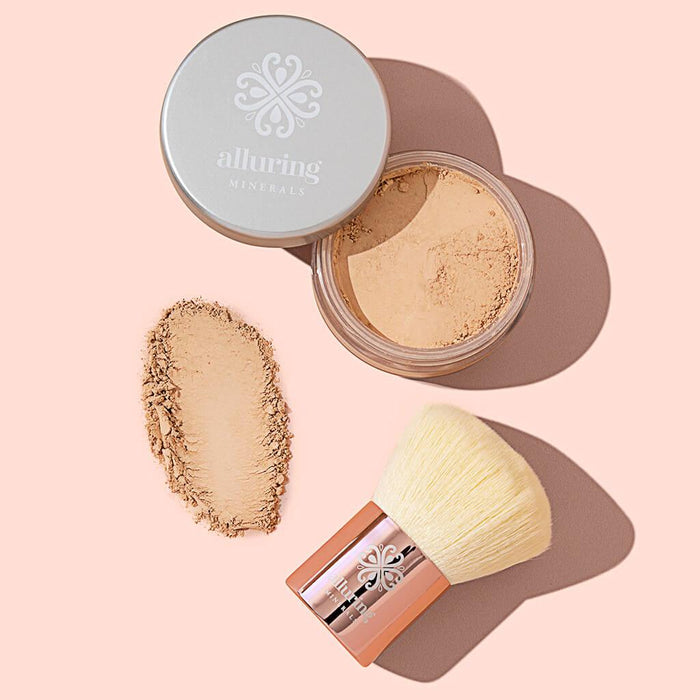 Open jar of Alluring Minerals Mineral Foundation Powder with a powder swatch and rose gold kabuki brush