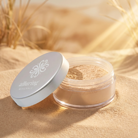 Open jar of loose powder with a white lid on sand, featuring the brand 'alluring'.