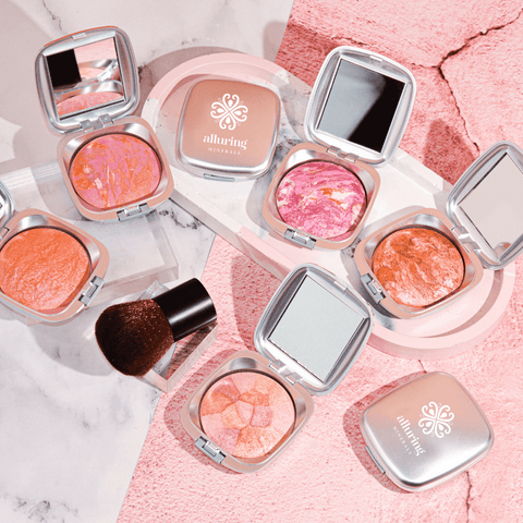 Alluring Minerals Mineral Baked Blush compacts styled with a kabuki brush on a pink background